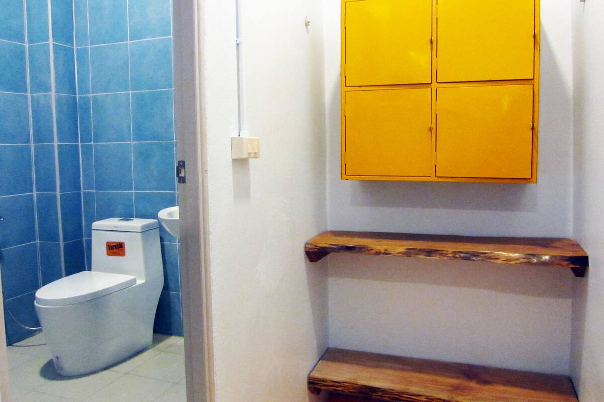 A bathroom with a toilet, a blue tiled wall, and a yellow cabinet.