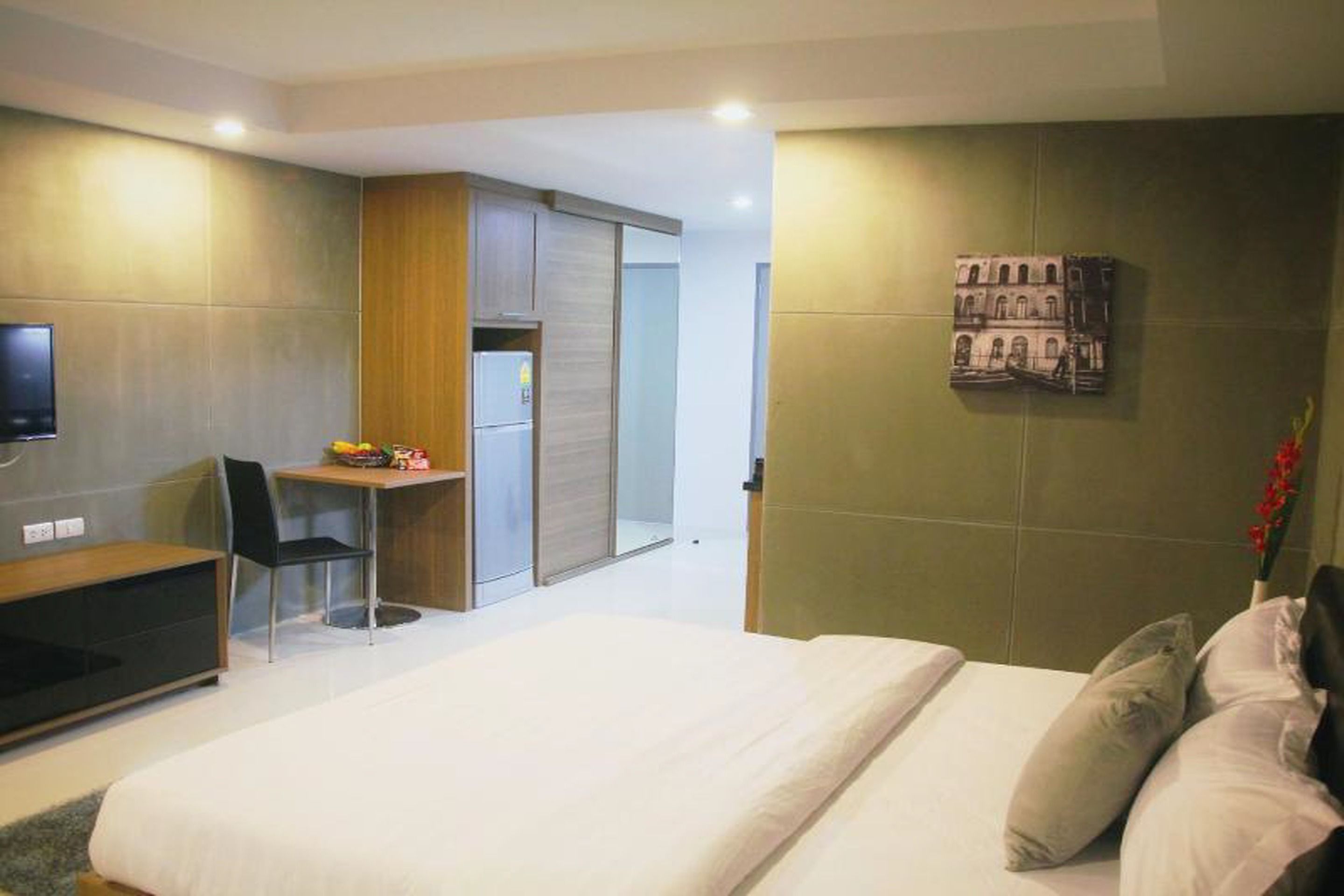 A modern hotel room with a bed, a desk, a chair, a television, and a small table with a fruit bowl.