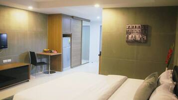 A modern hotel room with a bed, a desk, a chair, a television, and a small table with a fruit bowl.