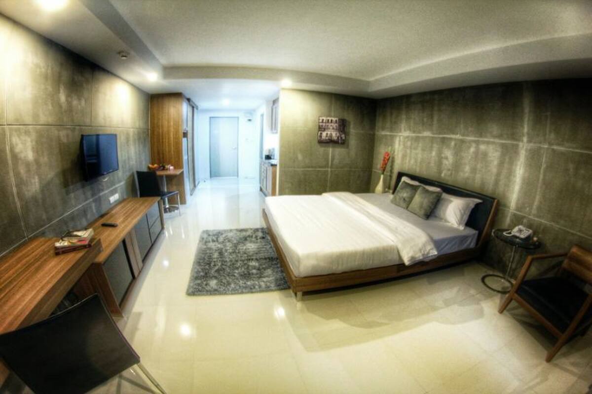Un dormitorio moderno con una cama grande, un televisor montado en la pared, un escritorio y una silla.