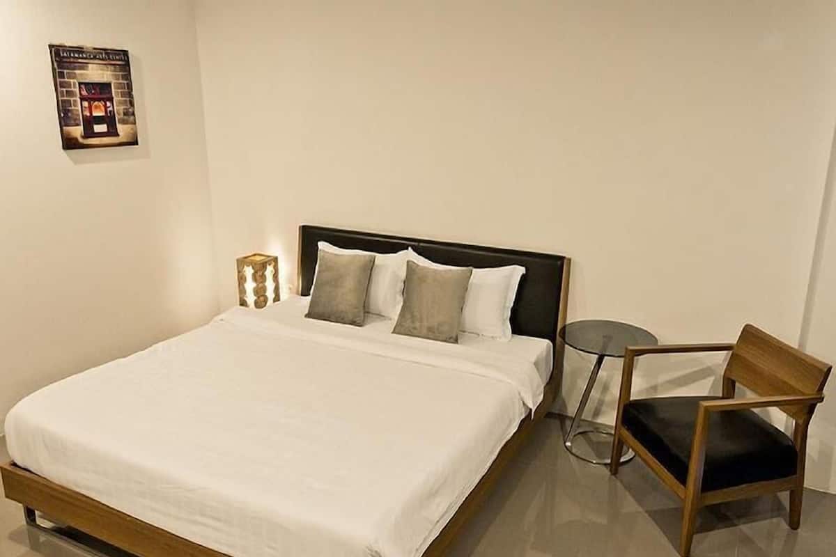 A hotel room with a bed, a chair, a bedside table, and a wall-mounted poster.