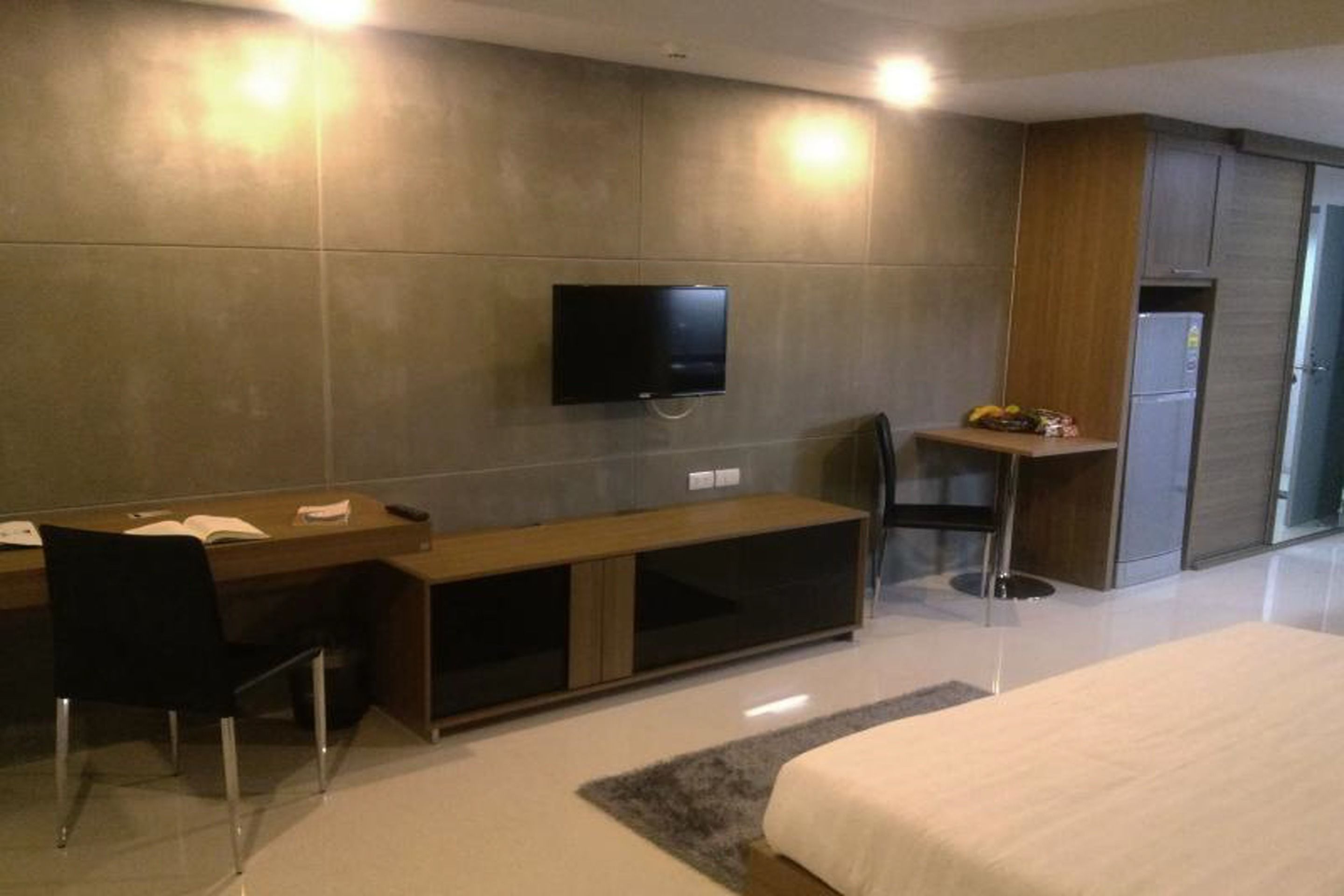 Une chambre d’hôtel moderne équipée d’un lit, d’un bureau avec une chaise, d’un téléviseur fixé au mur et d’un petit coin cuisine.