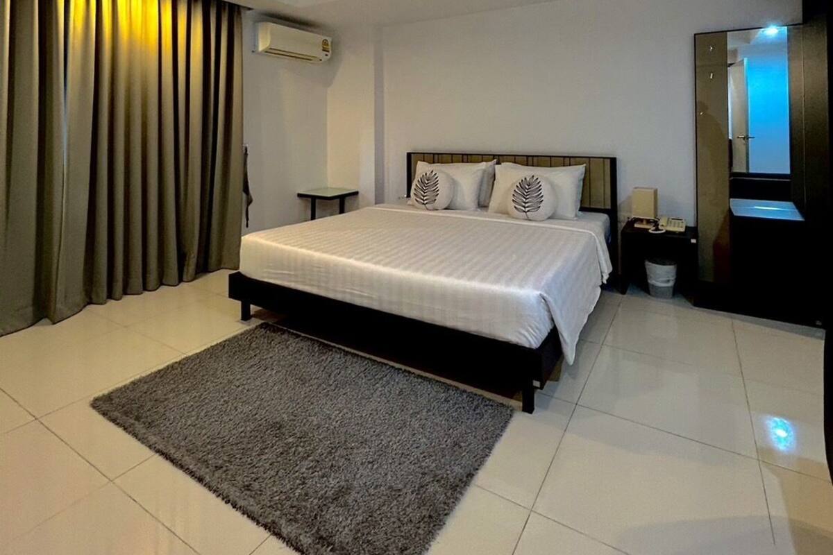 Una habitación de hotel moderna con una cama grande, una mesita de noche pequeña, una mesita auxiliar, un espejo y una ventana con cortinas.