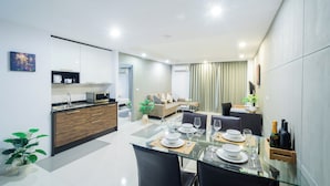 A modern kitchen with a dining area, white cabinetry, and a glass table set for four. - WE GRAND EVER 9 (Nakhon Ratchasima)