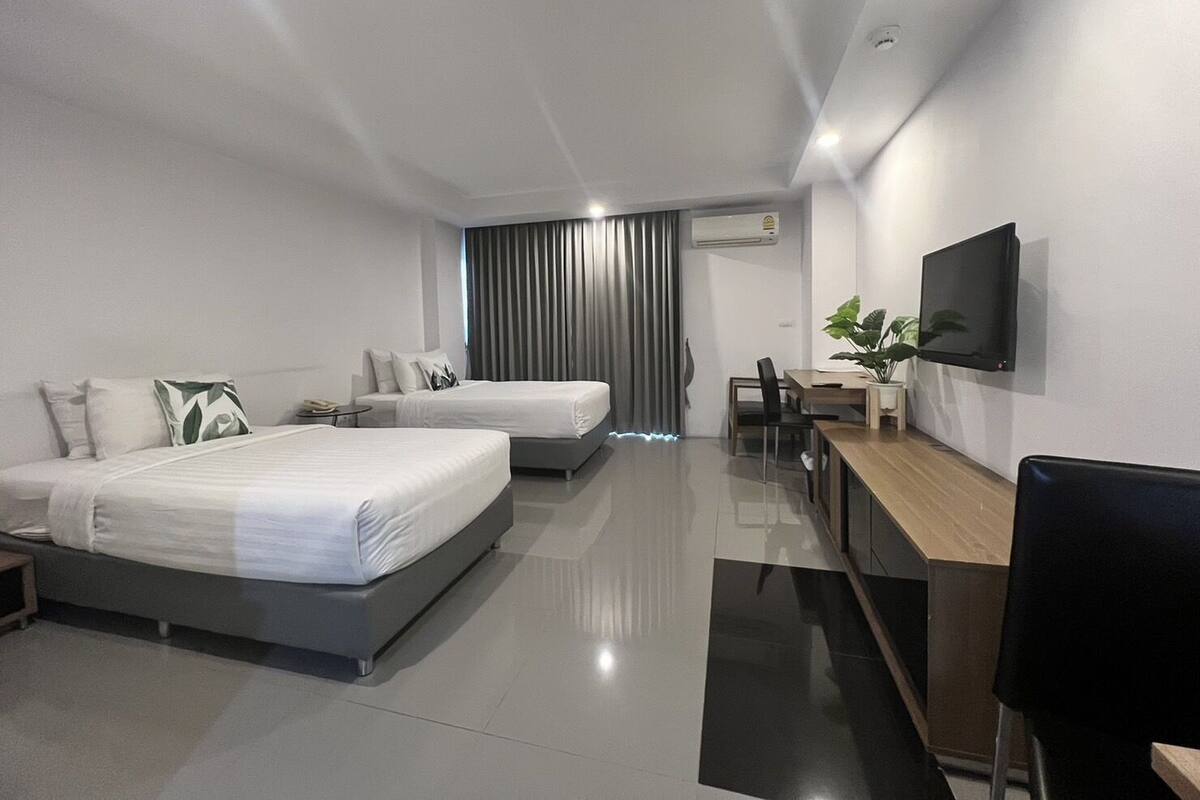 Una habitación de hotel moderna con dos camas, un escritorio, una silla, un televisor y una planta.