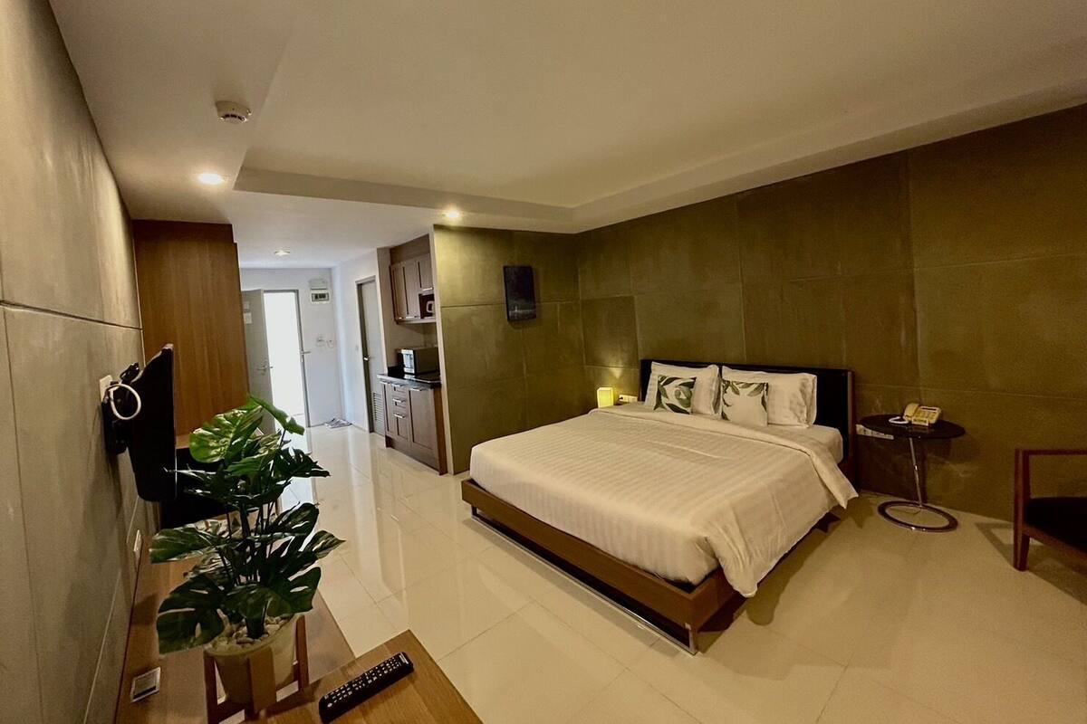Una habitación de hotel moderna con una cama grande, un televisor, una planta y una mesita de noche con un teléfono.