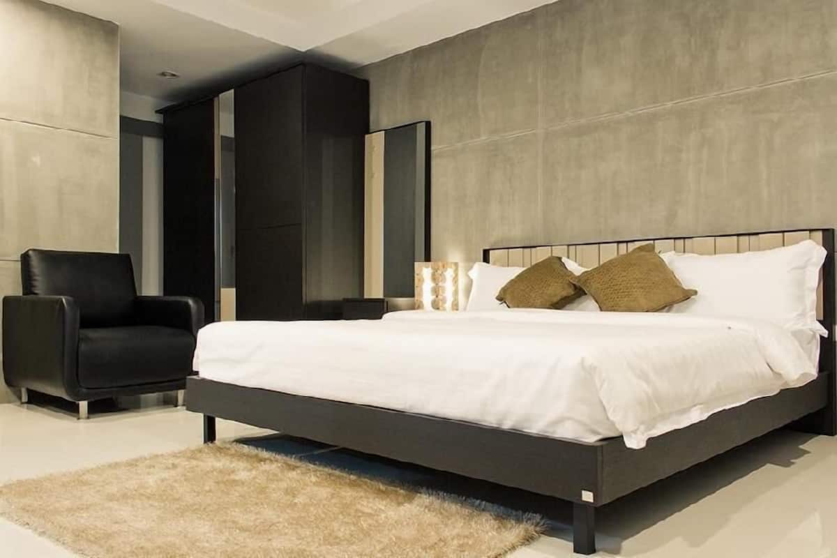 A modern bedroom with a large bed, a black chair, and a fluffy rug.