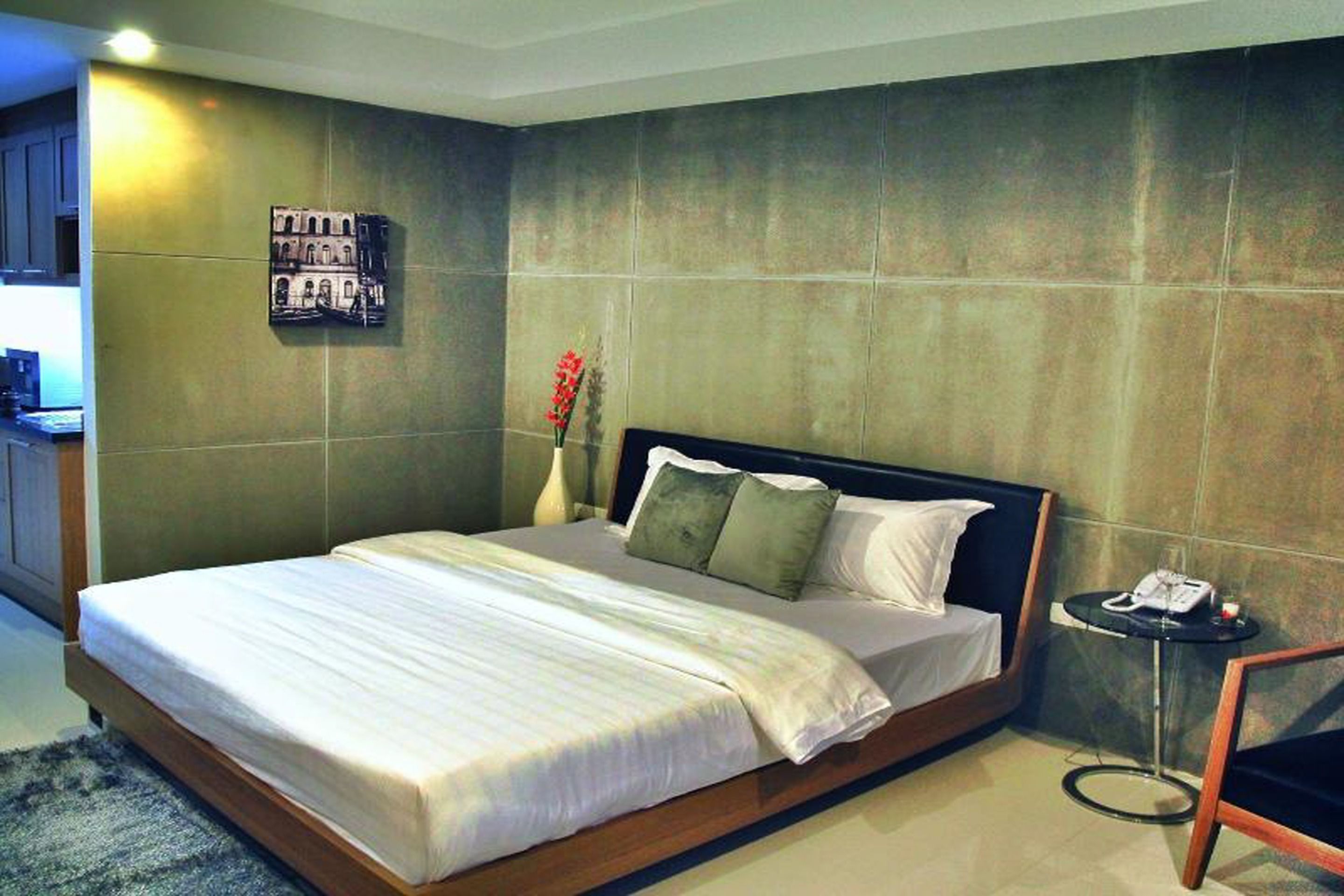 A modern hotel room with a large bed, a small bedside table, and a wall-mounted picture.