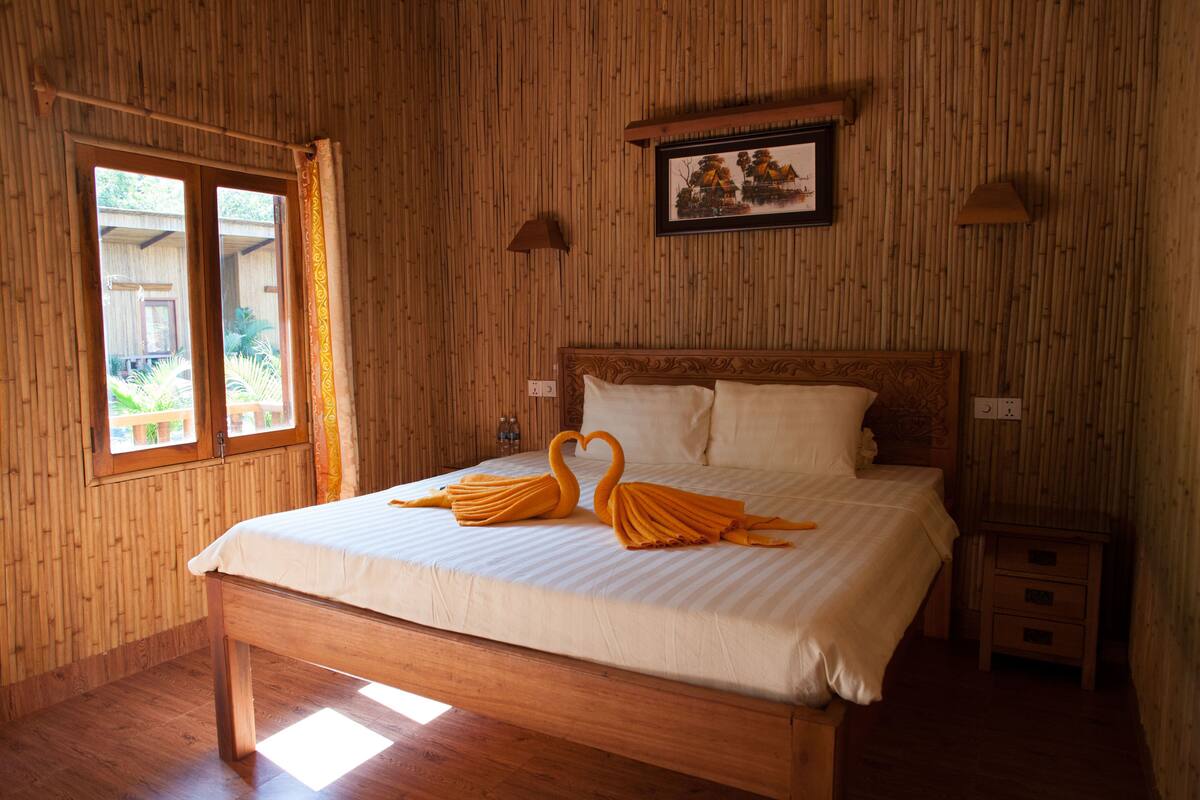 A wooden-paneled room with a bed, a framed picture on the wall, and a window with curtains.