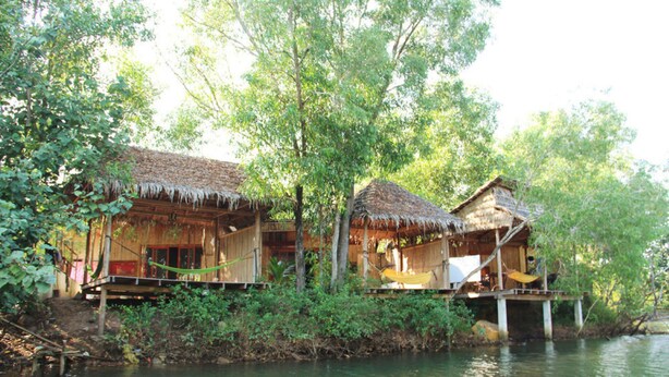 Una casa in legno con tetto di paglia, immersa nel verde lungo un fiume.