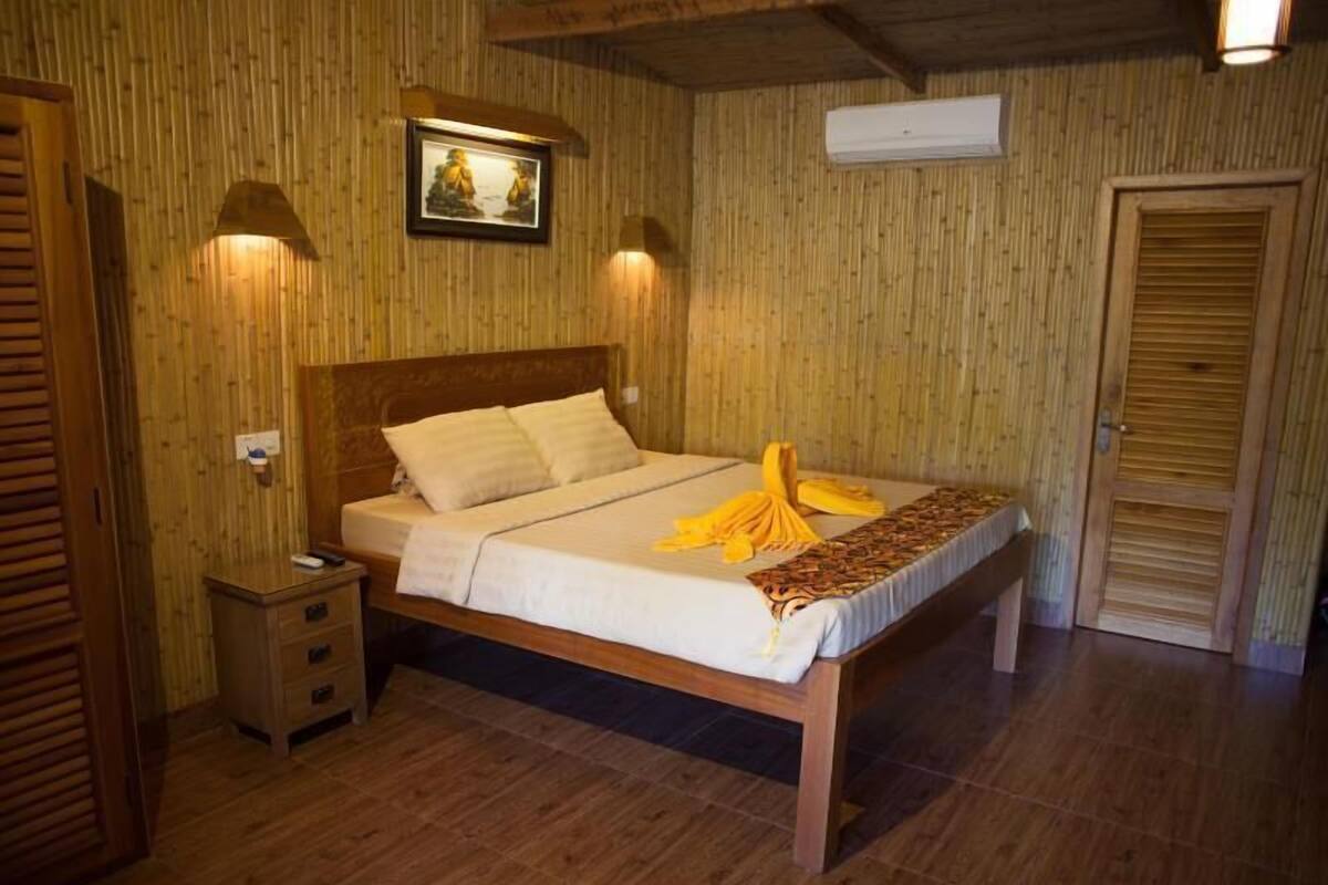 A wooden-framed bed with a white mattress and pillows, a bedside table with a lamp, and a framed picture on the wall.