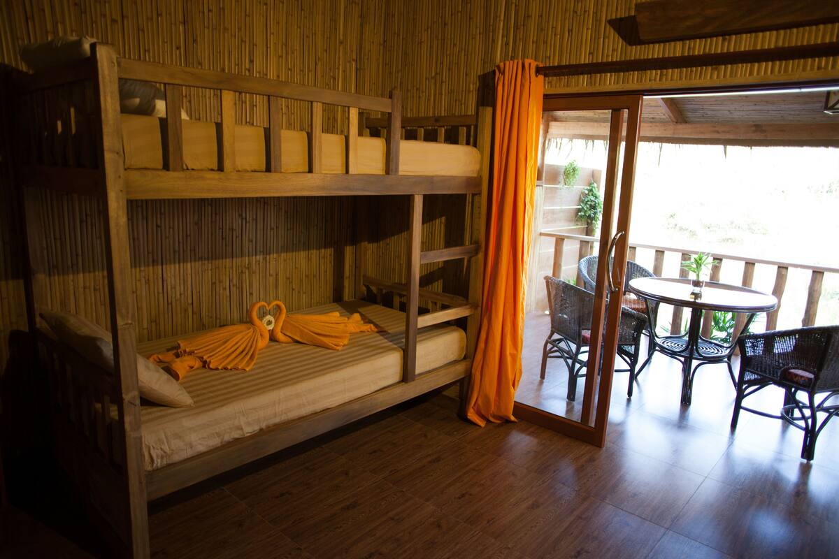 A bunk bed room with a wooden floor, a table with chairs, and a view of the outdoors through a glass door.