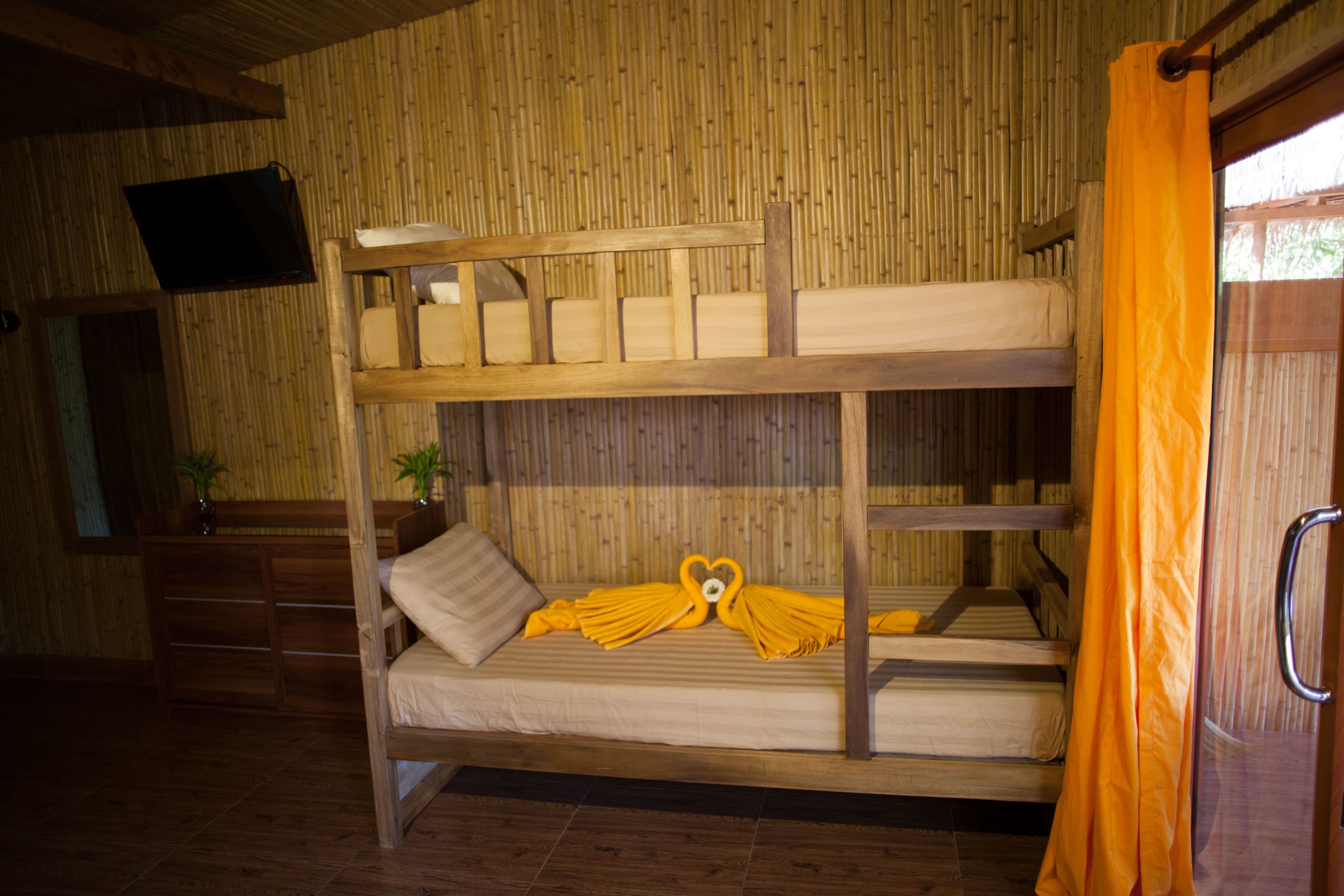 Ein Stockbett mit Holzrahmen, ein an der Wand befestigter Fernseher und ein Fenster mit orangefarbener Vorhang.