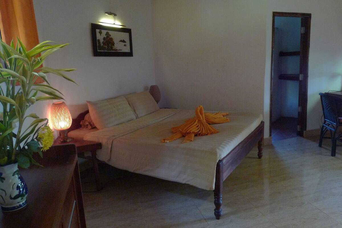 A room with a bed, a desk, a chair, a potted plant, and a wall-mounted lamp.