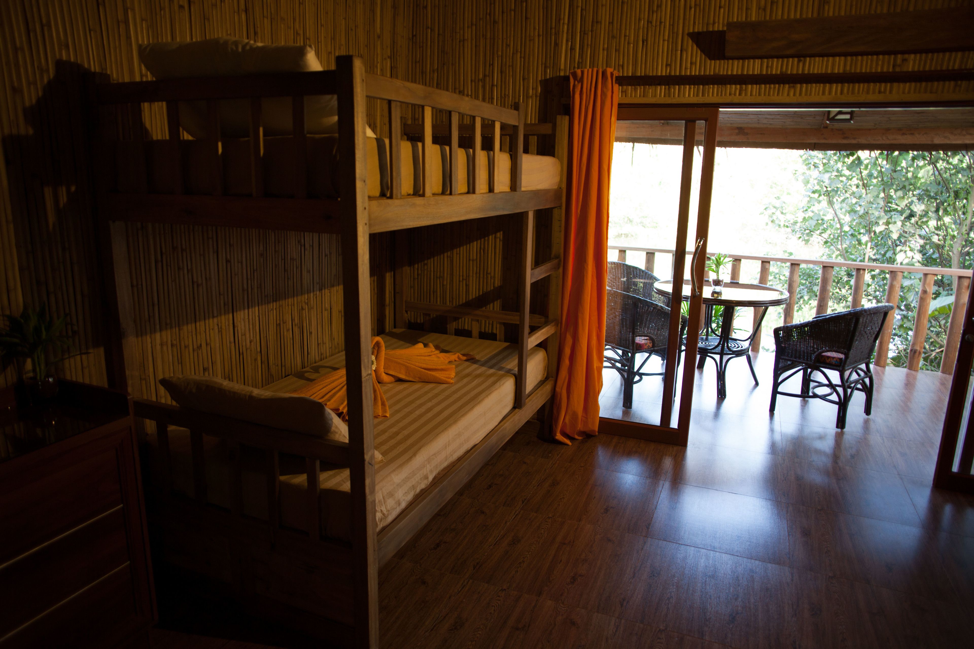 A room with bunk beds, a small table, and chairs. There is a balcony with a table and chairs outside.