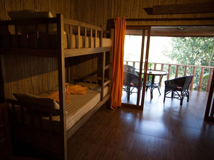 A room with bunk beds, a small table, and chairs. There is a balcony with a table and chairs outside.
