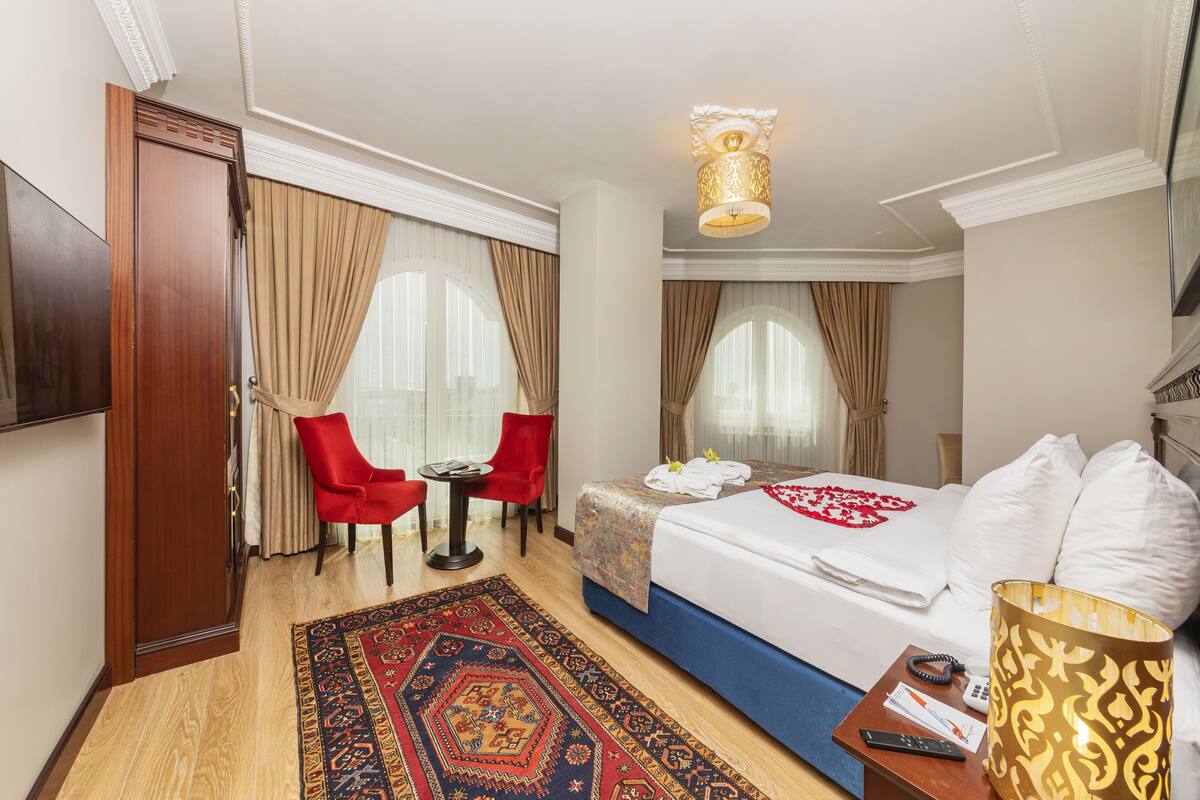 Ein Hotelzimmer mit Bett, Schreibtisch, Stuhl, Fernseher und einem großen Fenster mit Vorhängen.