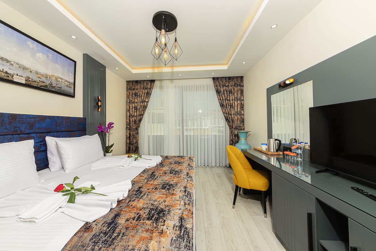 Ein modernes Hotelzimmer mit Bett, Schreibtisch mit Fernseher, großem Fenster mit Vorhängen und einem Gemälde an der Wand.
