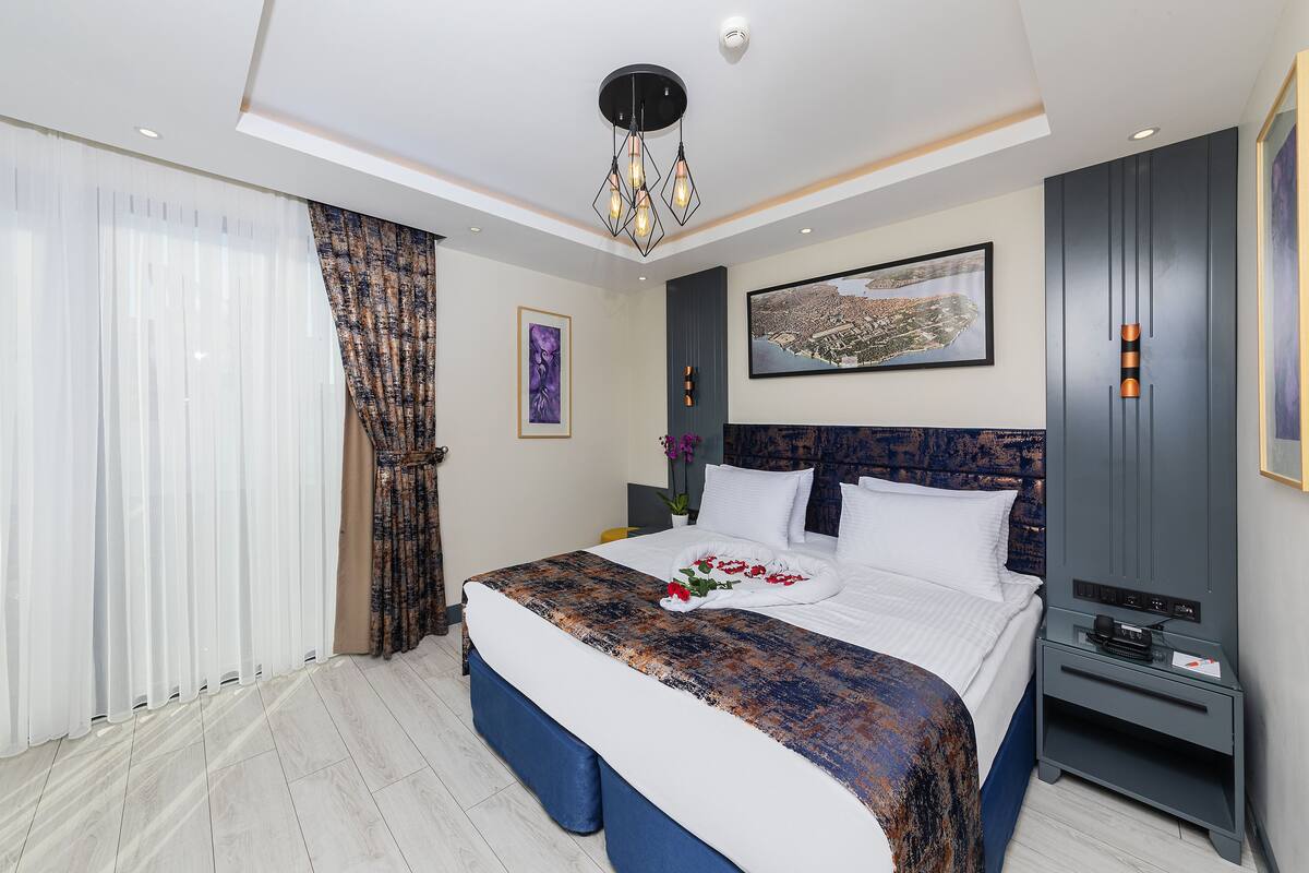 Ein modernes Hotelzimmer mit einem großen Bett, einem Nachttisch, einem Schreibtisch und einer Deckenleuchte.