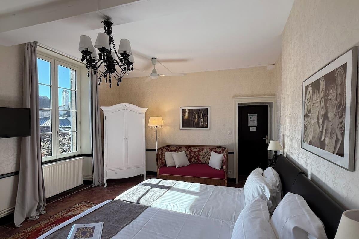 Une chambre d’hôtel avec un grand lit, une armoire, un canapé, un lustre et un tableau au mur.