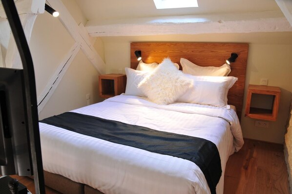 A bedroom with a wooden headboard, white bedding, a fluffy pillow, and bedside tables with lamps.