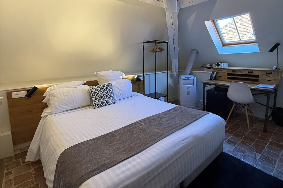 Une chambre à coucher comprenant un lit, un bureau, une chaise, une fenêtre et un puits de lumière.