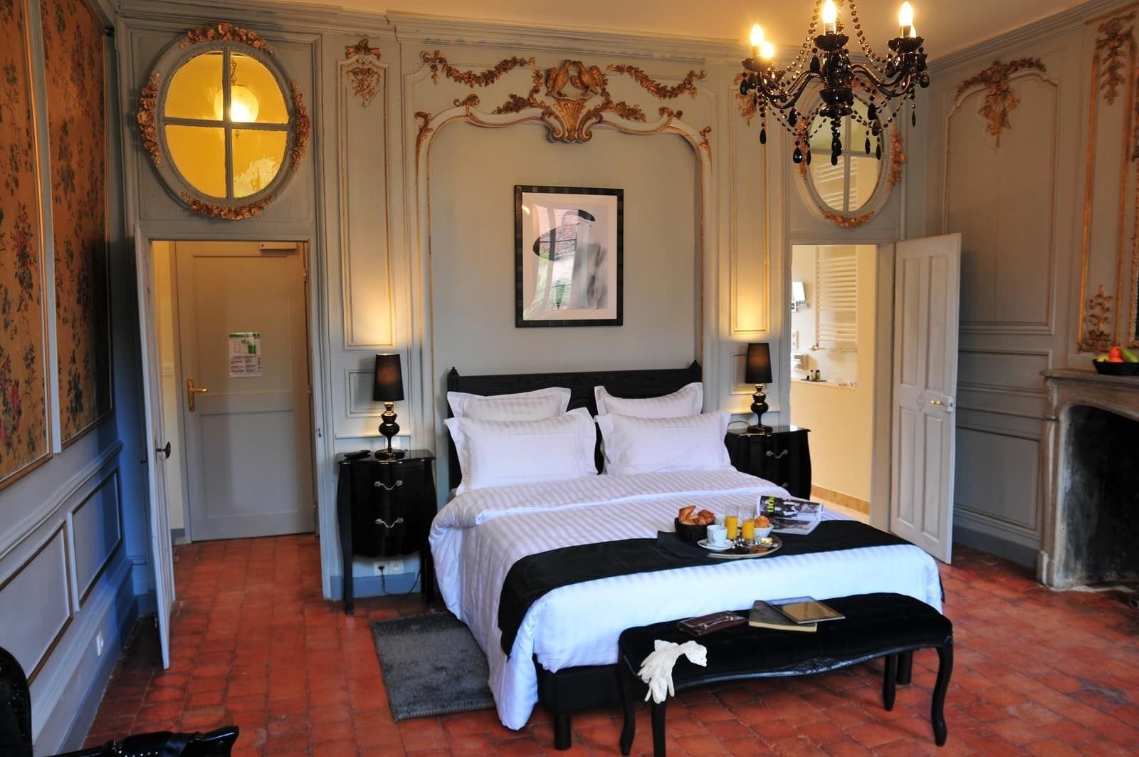 Quarto de hotel clássico com uma cama grande, duas mesas de cabeceira, um candelabro e uma lareira.