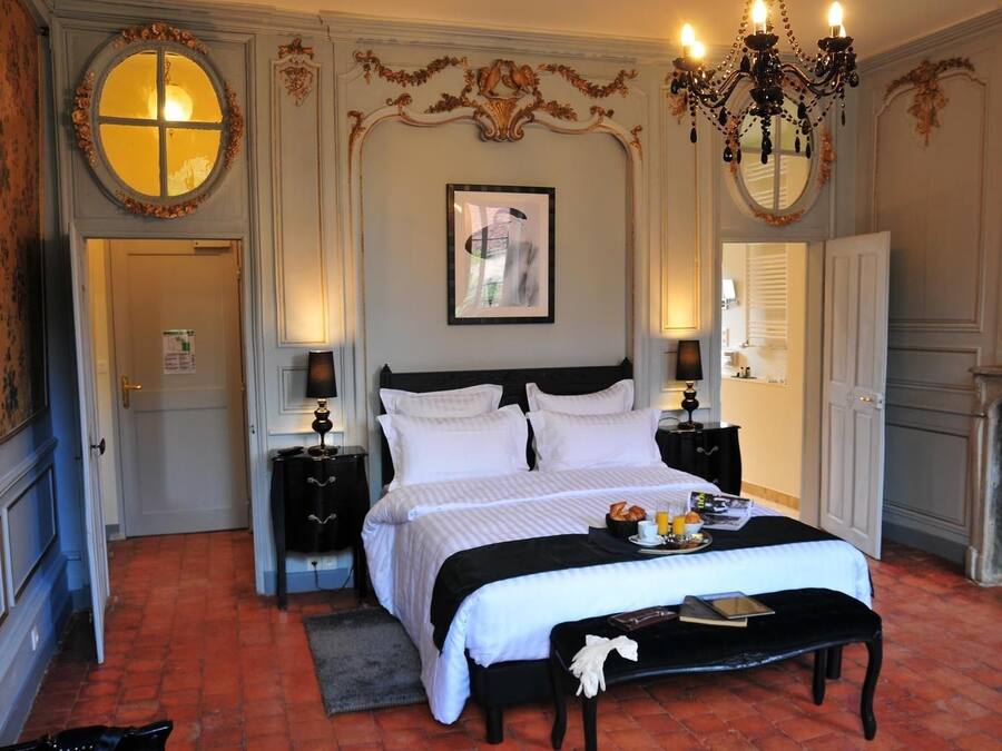 Una habitación de hotel clásica con una cama grande, dos mesitas de noche, un candelabro y una chimenea.