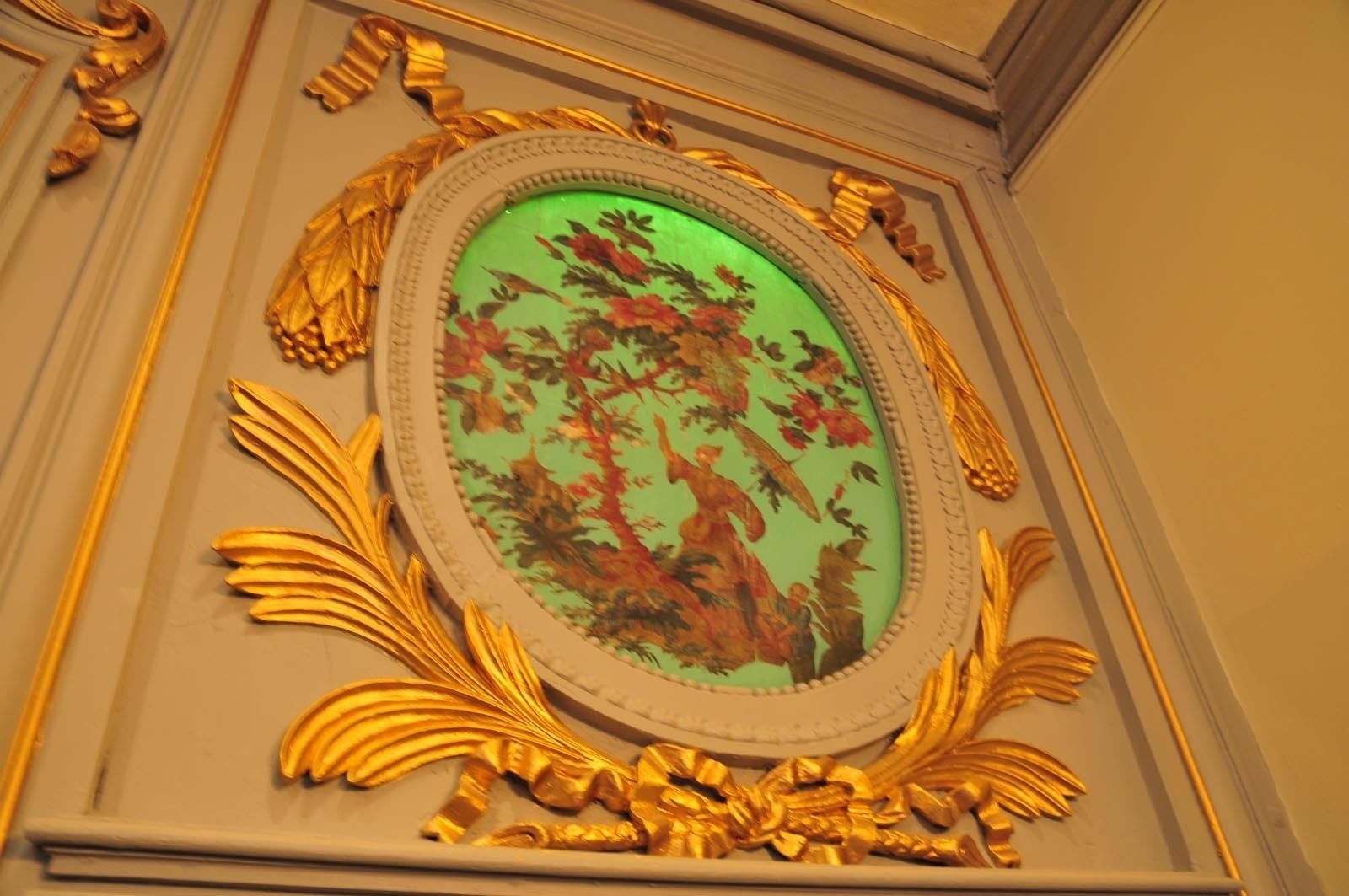 An ornate, oval-framed mirror with a green background and floral design.