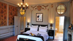 A spacious bedroom with a large bed, a chandelier, a fireplace, and a view of the outside.