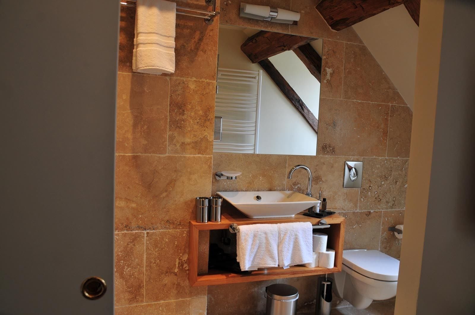 Un baño con pared de piedra, tocador de madera, lavabo blanco y retrete.
