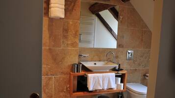 Un baño con pared de piedra, tocador de madera, lavabo blanco y retrete.