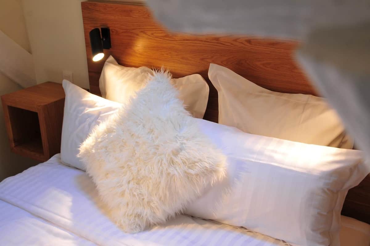 Un lit bien fait, avec du linge de lit blanc et des oreillers moelleux, une tête de lit en bois et une table de chevet avec une lampe.