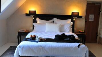 A neatly made bed with white linens, a black headboard, and two bedside lamps. There is a tray with croissants and a cup on the bed.