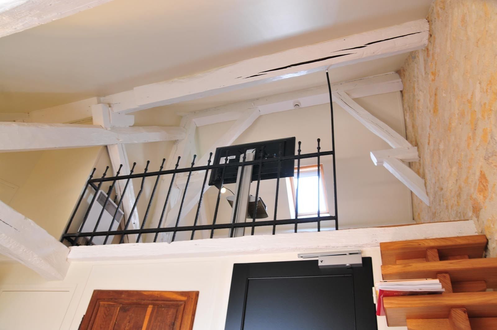 A room with a wooden door, a black door, a window with a view, and a black metal railing.