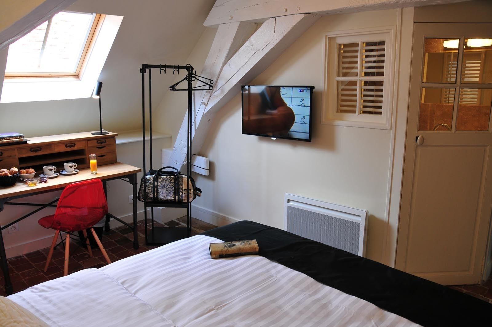 A bedroom with a bed, a desk with a chair, a TV, and a window.