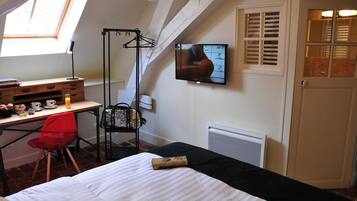A bedroom with a bed, a desk with a chair, a TV, and a window.