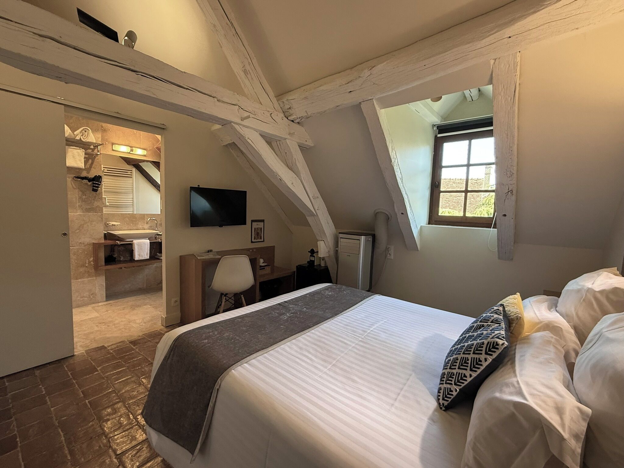 Quarto com cama, escrivaninha, cadeira, televisão e janela.