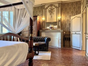 Een slaapkamer met een hemelbed, een leren bank en een eethoek met een tafel en stoelen.