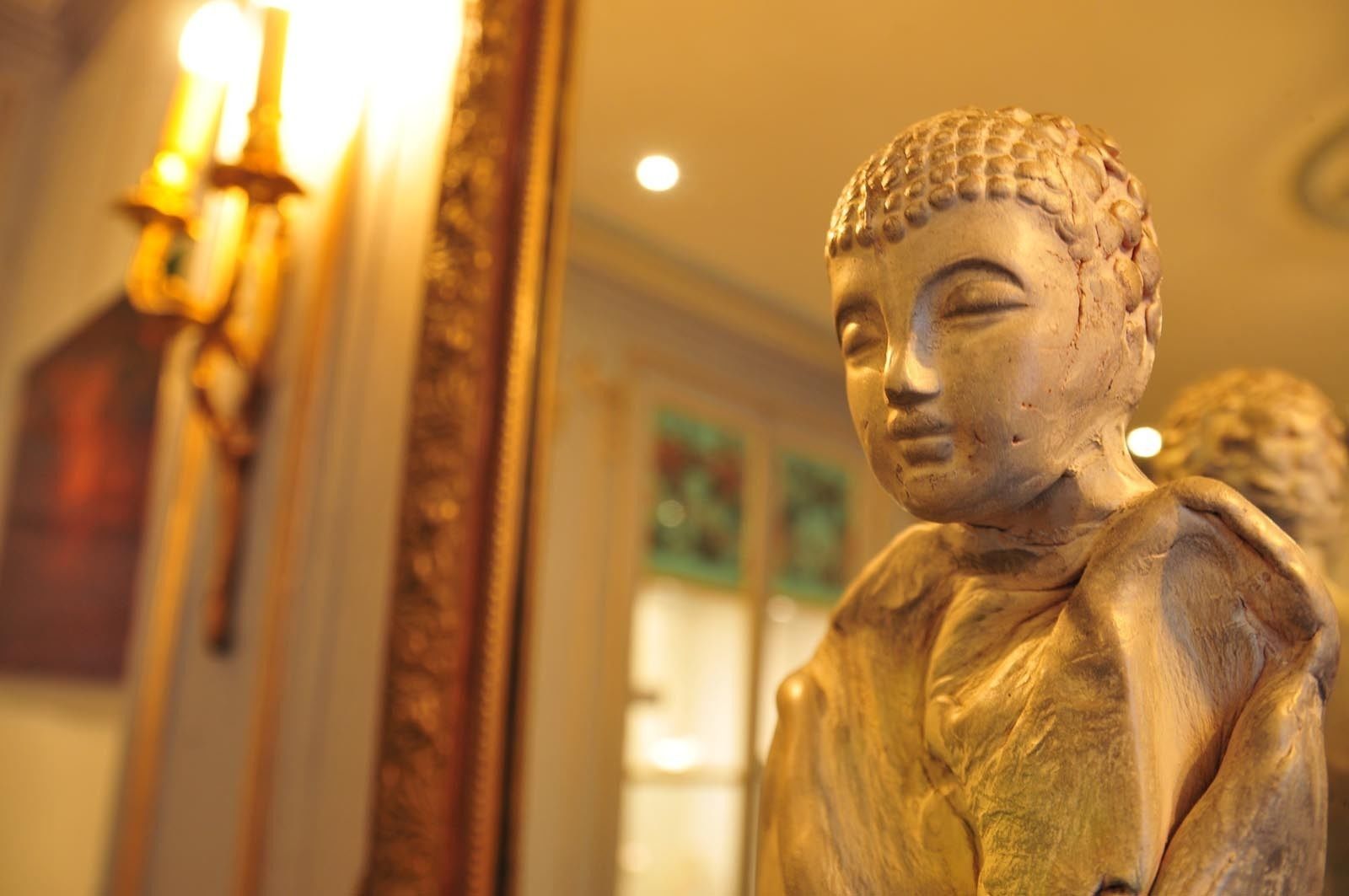 Una estatua en un cuarto con luz cálida, con un espejo que refleja parte de la estatua.