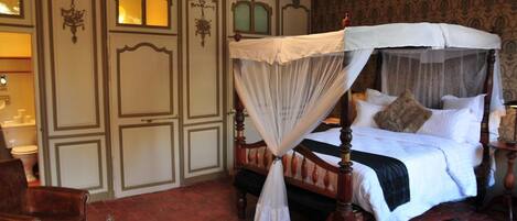 A four-poster canopy bed with a white bedspread and pillows, a wooden headboard, and a red rug on a red brick floor.
