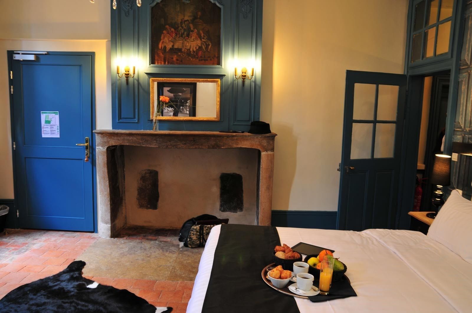 A hotel room with a bed, breakfast tray, a fireplace, and a painting above the mantel.