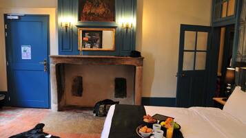 A hotel room with a bed, breakfast tray, a fireplace, and a painting above the mantel.