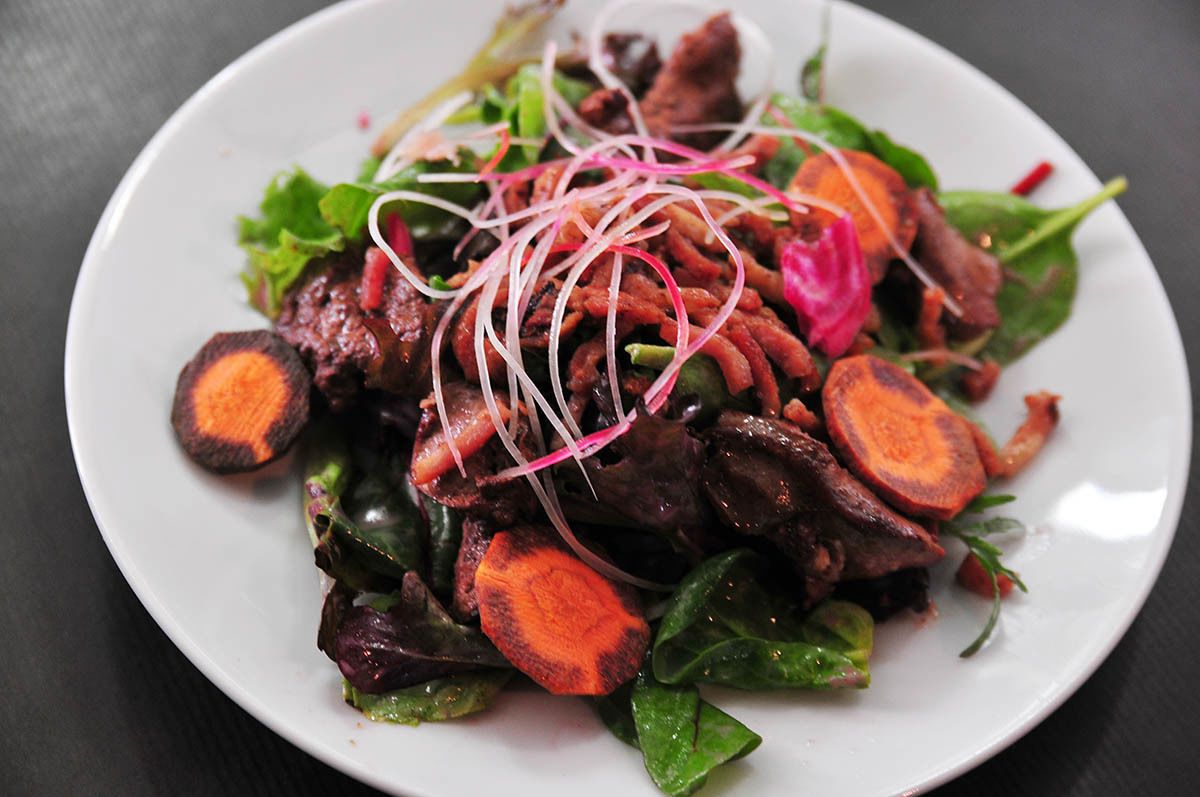 A plate of food with sliced carrots, leafy greens, and possibly meat, garnished with thinly sliced red onions.