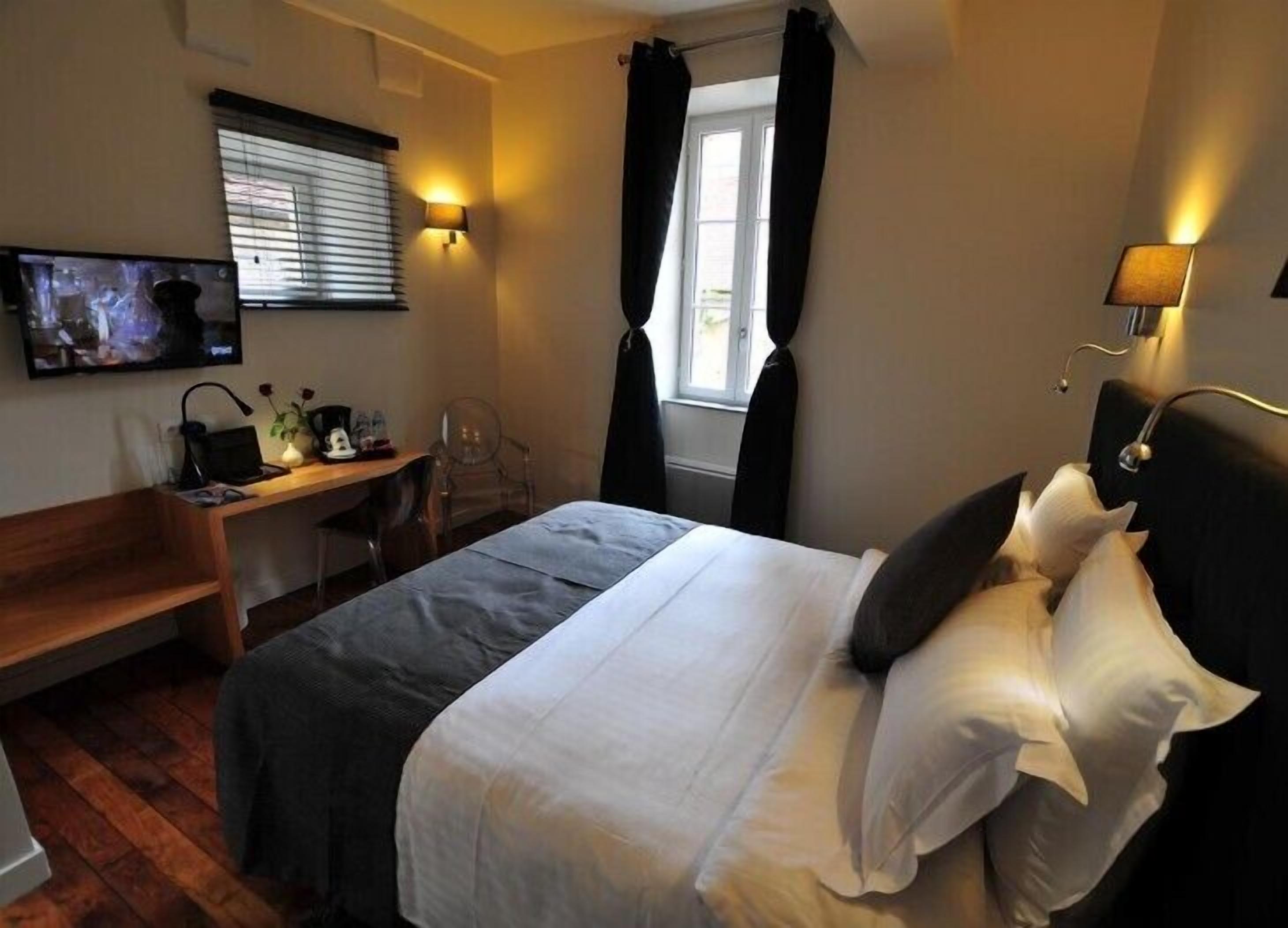 A hotel room with a bed, a desk, a chair, a television, and a window with curtains.