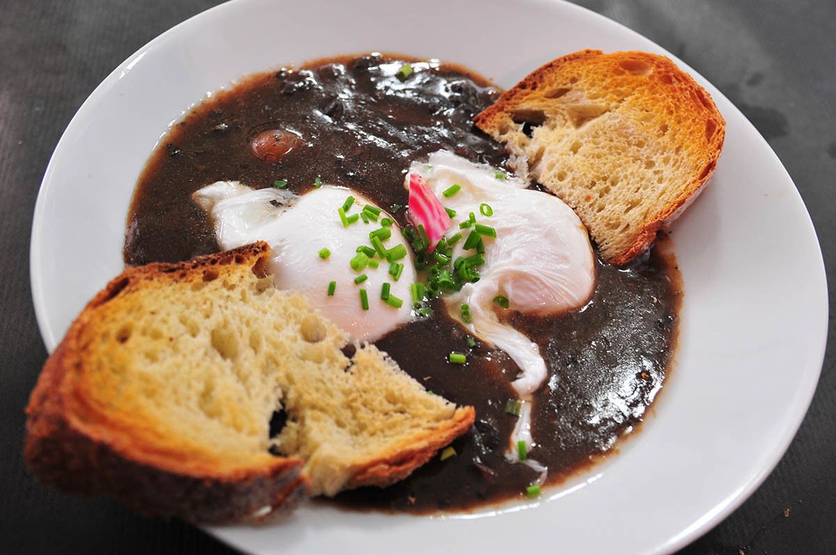 A plate of food with a poached egg, black sauce, and toasted bread.