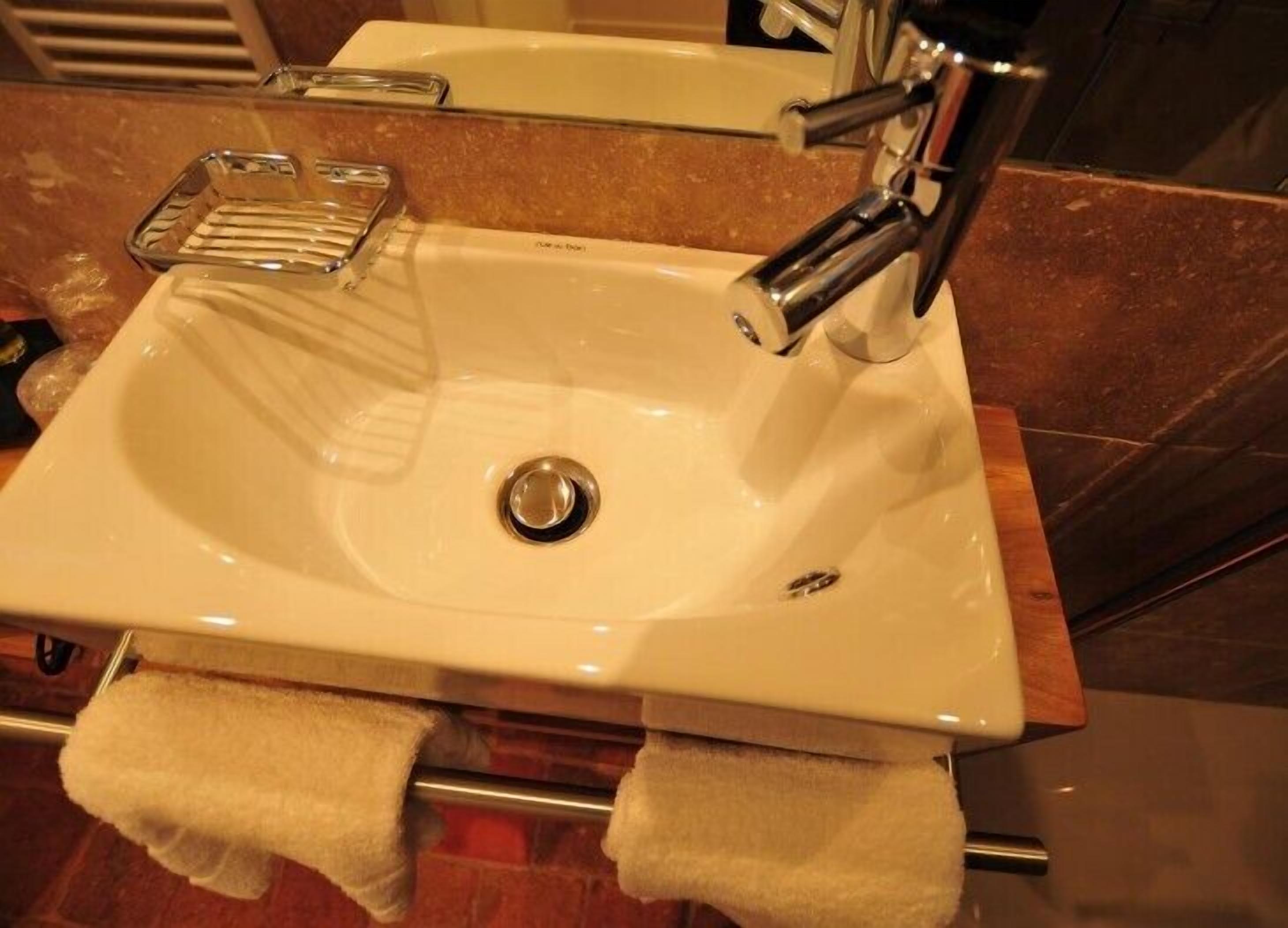 A white bathroom sink with a chrome faucet, a glass soap dish, and two towels hanging on a towel rack.