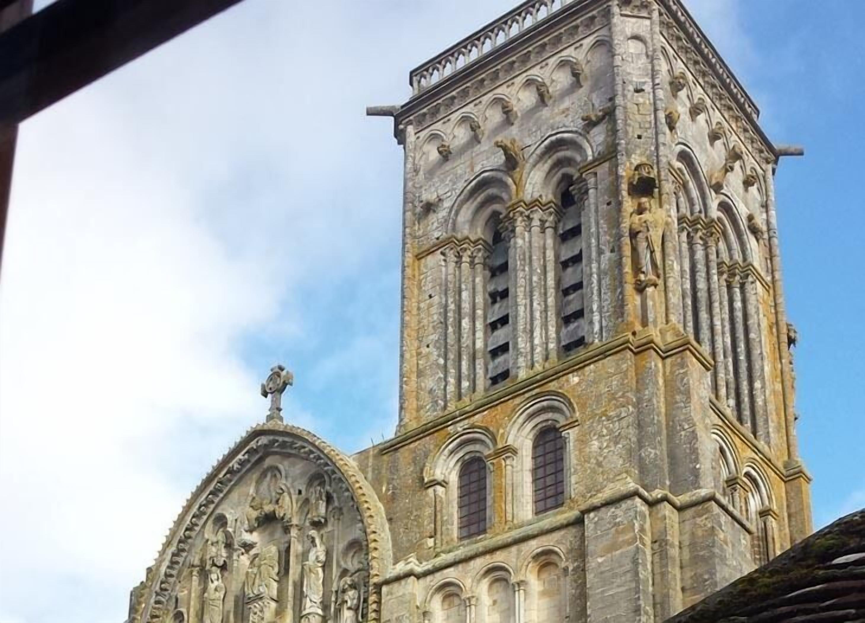 A historic stone building with a tall tower featuring arched windows and intricate carvings.