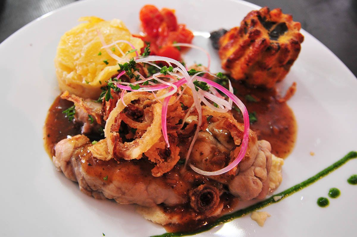 A plate of food with a variety of dishes including a main meat dish, a side of mashed potatoes, and a side of what appears to be a tomato-based sauce.