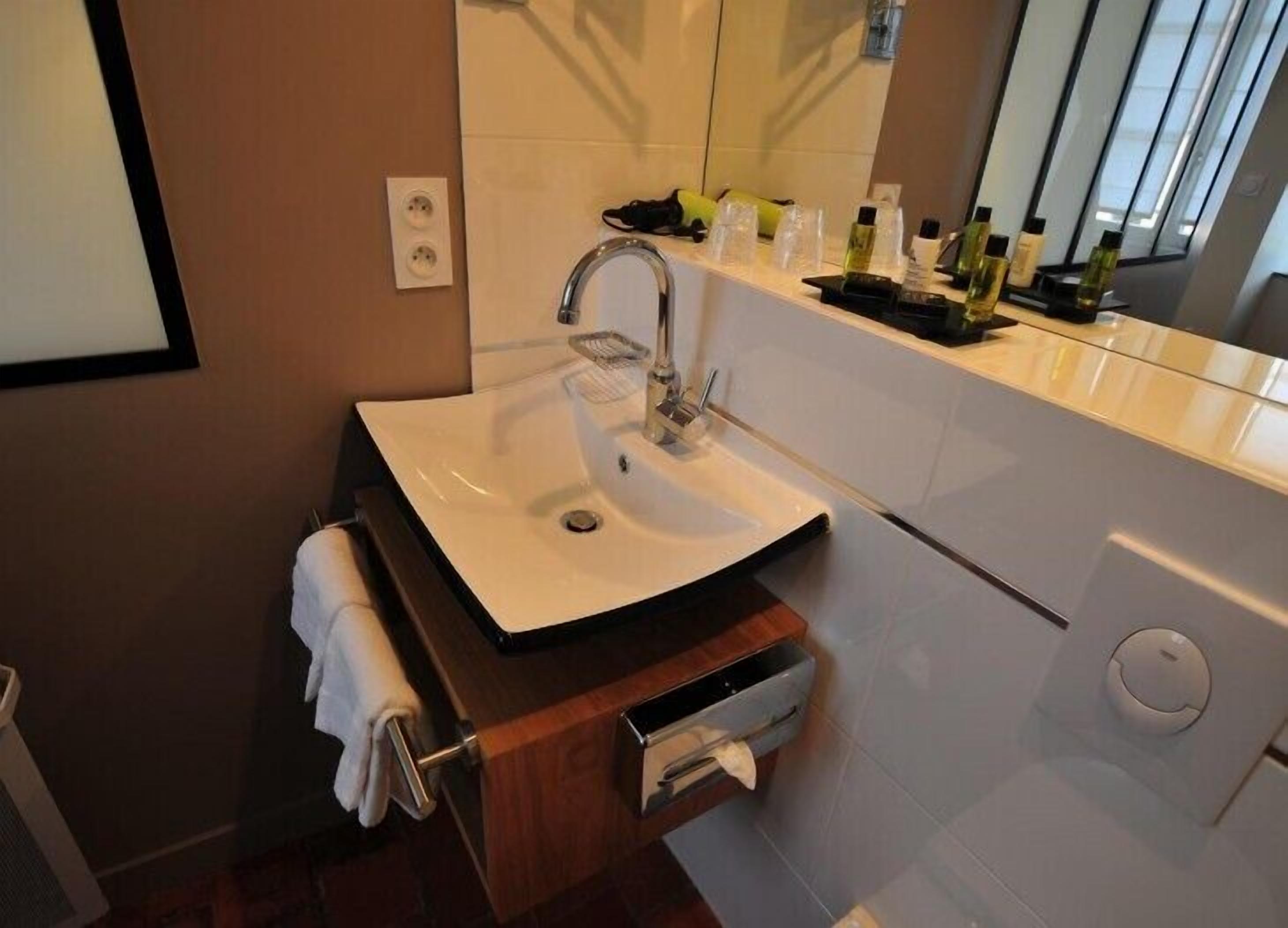 Une salle de bain moderne avec un lavabo blanc, un miroir et des articles de toilette posés sur le comptoir.